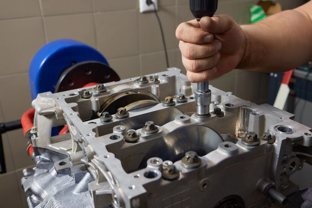 A person uses a power tool to tighten bolts on an exposed engine block during a gearbox repair in a workshop setting.