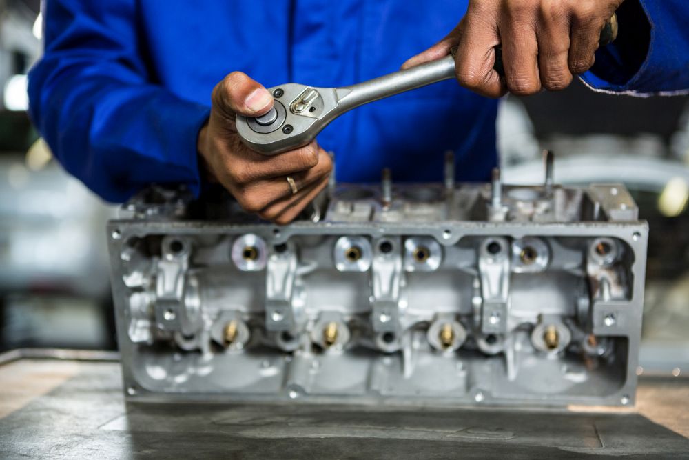 A person in a blue uniform uses a ratchet wrench to work on a metal engine component placed on a table, showcasing professional gearbox repair services.